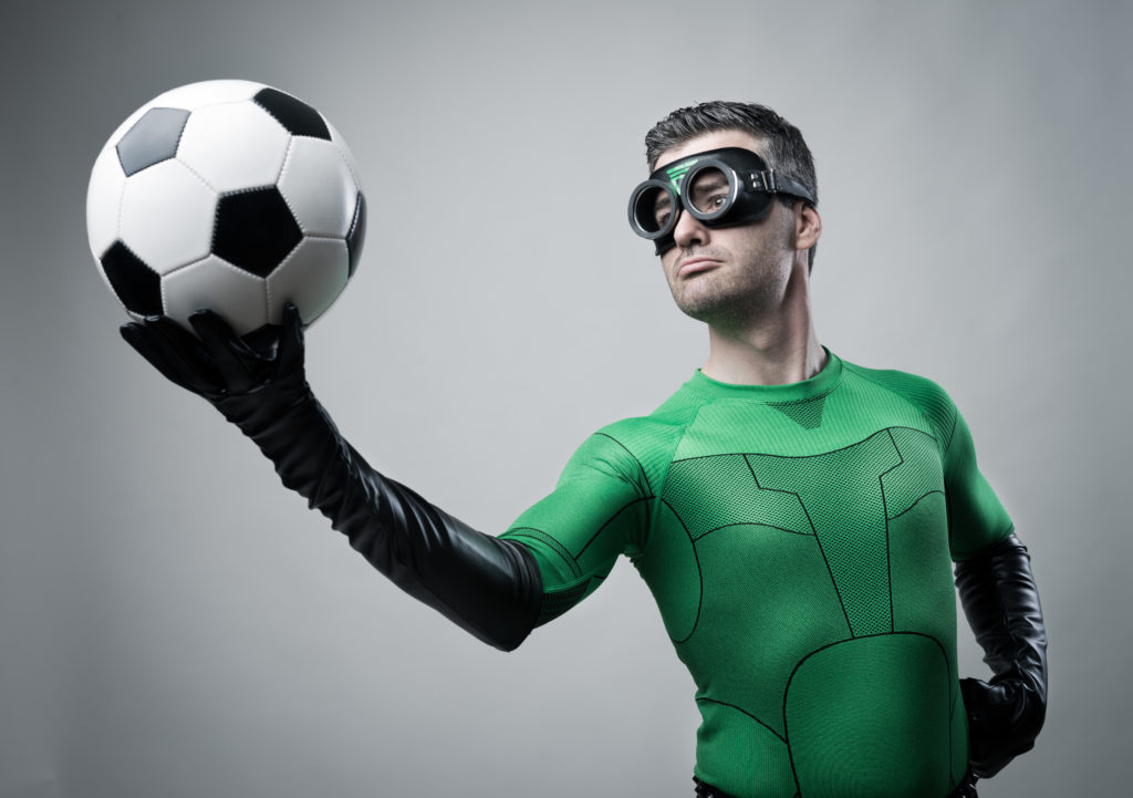 Confident superhero in green costume holding a soccer ball.