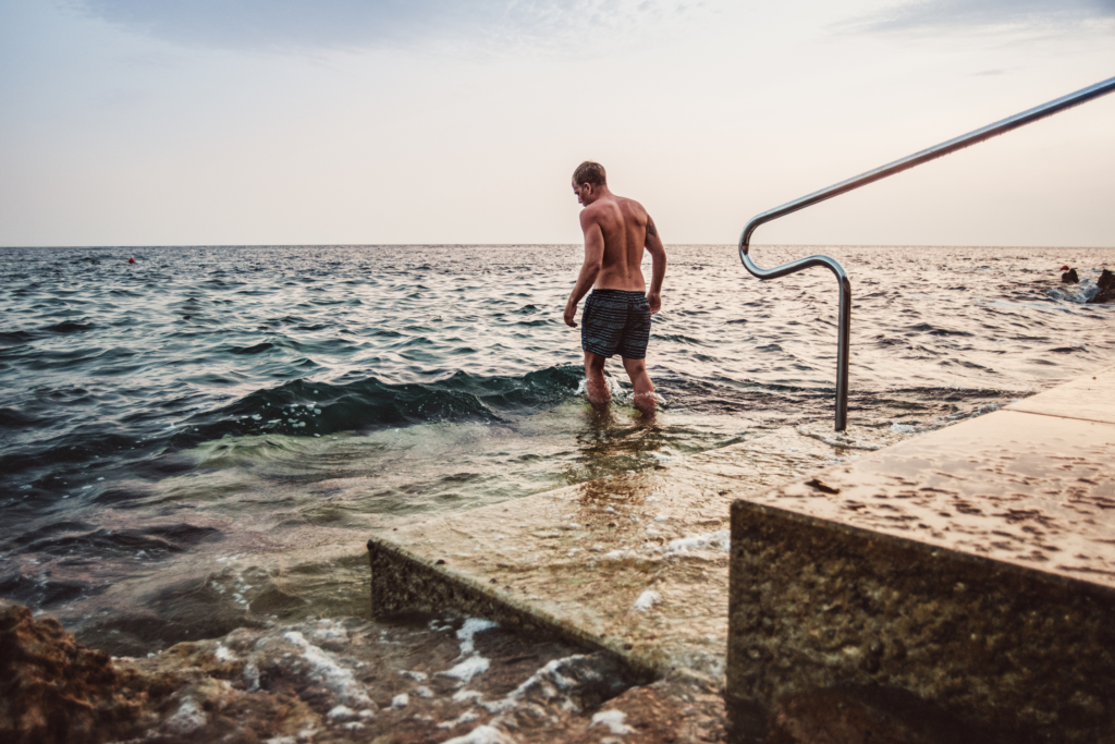 man walking into ocean off concrete steps